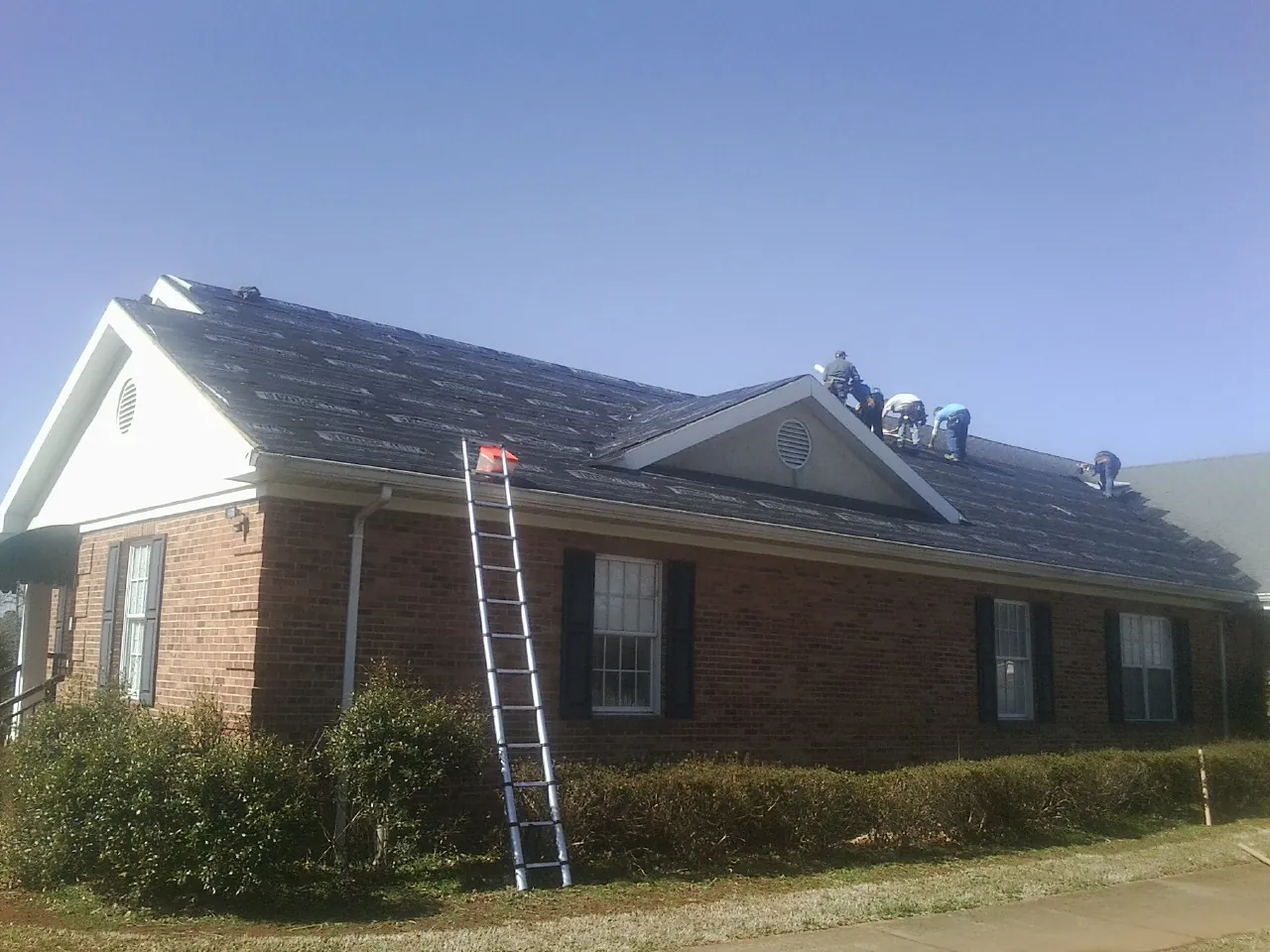 Crew tearing shingles off a brick ranch roof with a ladder set — Emergency Roof Repair work by our crew in Solomons