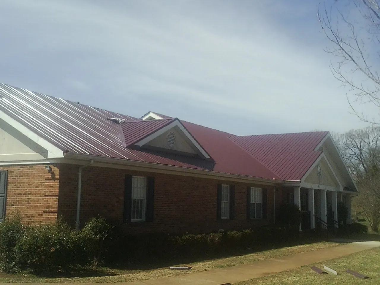 Red metal roof with gabled entries on a long brick building, from a Hail Damage Roof Repair job in Solomons