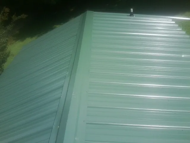 New green metal panels meeting at the ridge of a roof — Flat Roof Repair work by our crew in Solomons